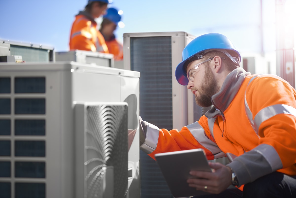 Energy assessor inspecting air conditioning units for a TM44 report